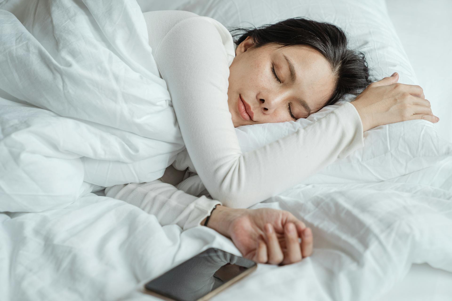Slapende vrouw in bed met mobiele telefoon
